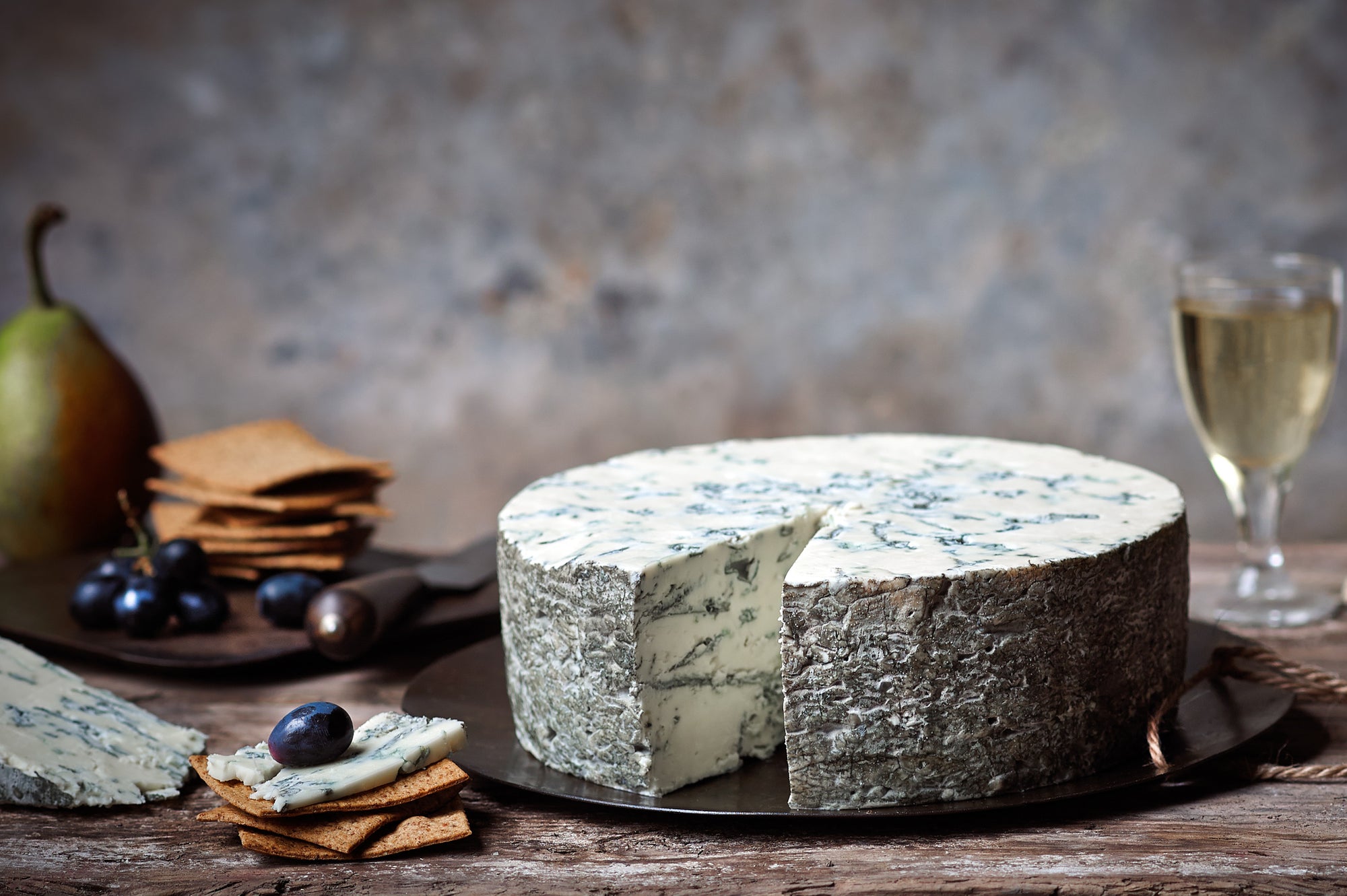 A full round of delicious, creamy, Buffalo Blue cheese by Shepherds Purse served on a rustic board with pears, crackers and grapes.